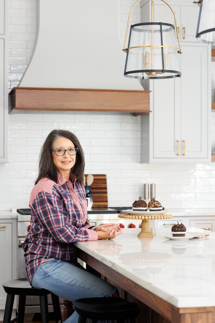 Jennifer Looney of JL Signature Designs sitting at the white marble top island of the kitchen she remodeled in Alpharetta, GA.