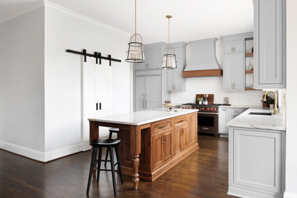Wide view of a remodeled luxury kitchen in Alpharetta with a dark wood island, white marble countertops, light gray custom cabinets, and gold pendant lighting over the seating area.