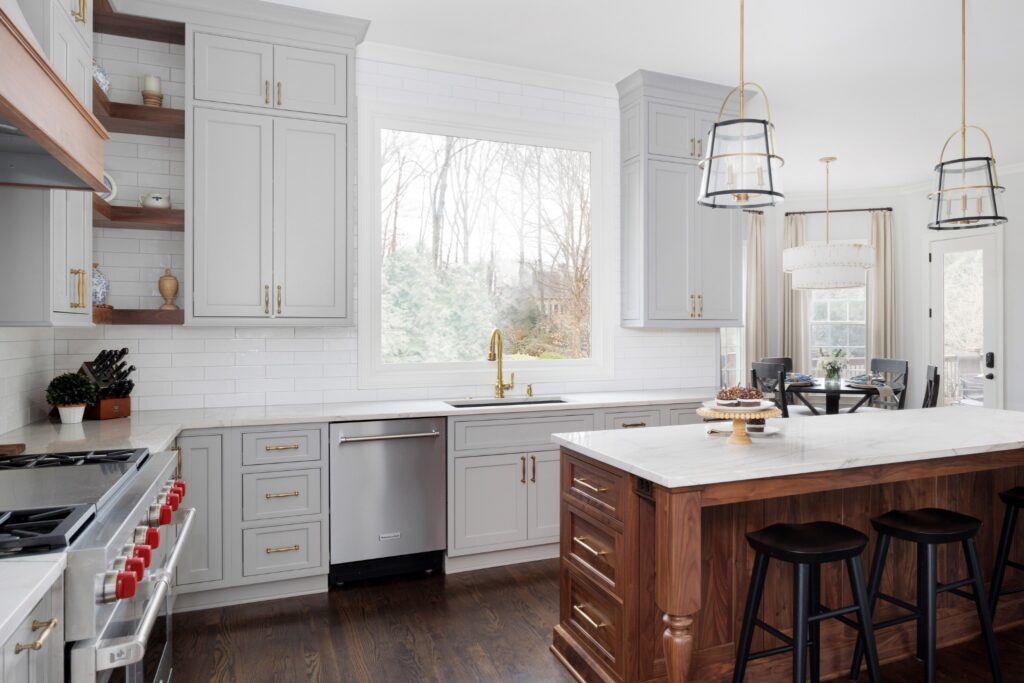 A bright, remodeled kitchen in Alpharetta featuring a large wood island with a marble countertop, gray cabinetry with gold hardware, and a matching white tile backsplash under a large window.