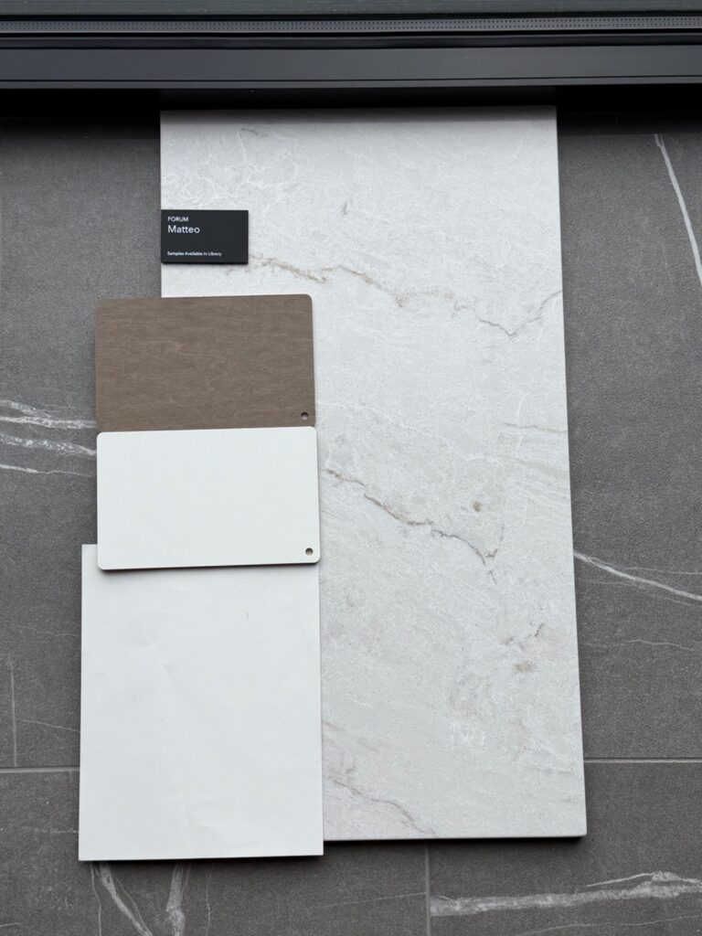 A close-up flat lay of interior design samples featuring a dark wood-textured plank, two crisp white quartz or stone samples, and a large gray marble-veined porcelain tile.