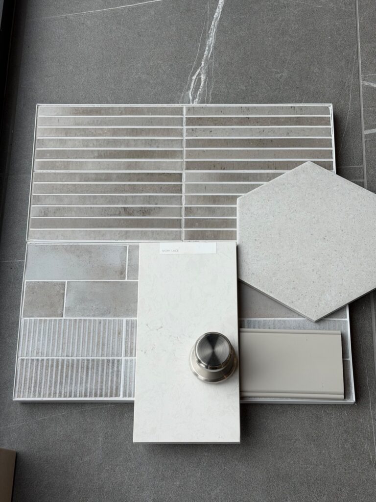 A flat lay of interior design material samples featuring gray marble-look tile, a section of thin horizontal mosaic tiles in neutral tones, and a large light gray hexagonal floor tile.