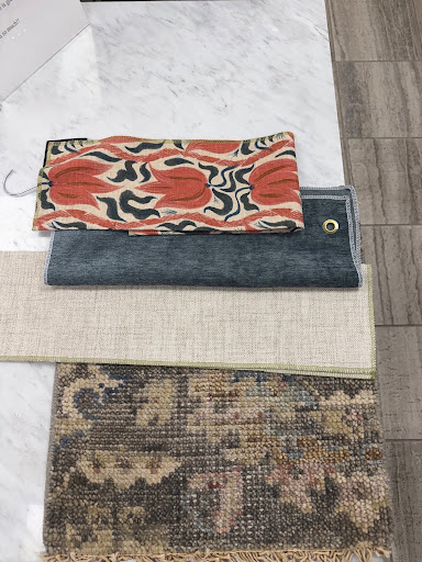 Flat lay arrangement of interior design material samples, including pattern fabric swatches, wood floor samples, a grey textile swatch, and a vintage-style patterned area rug.